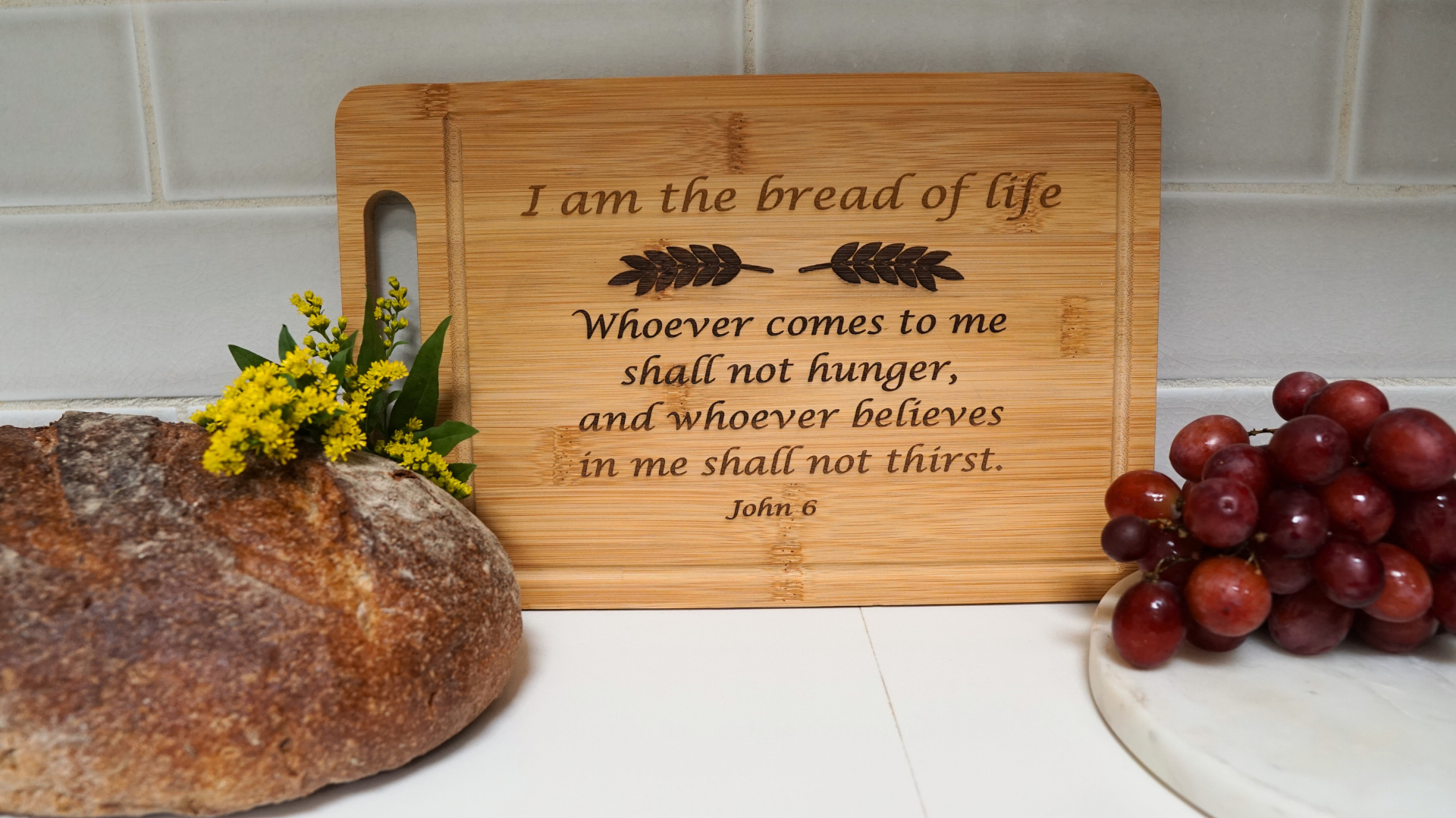 Bread board with engraved scripture "I am the bread of life" with bread and grapes on counter
