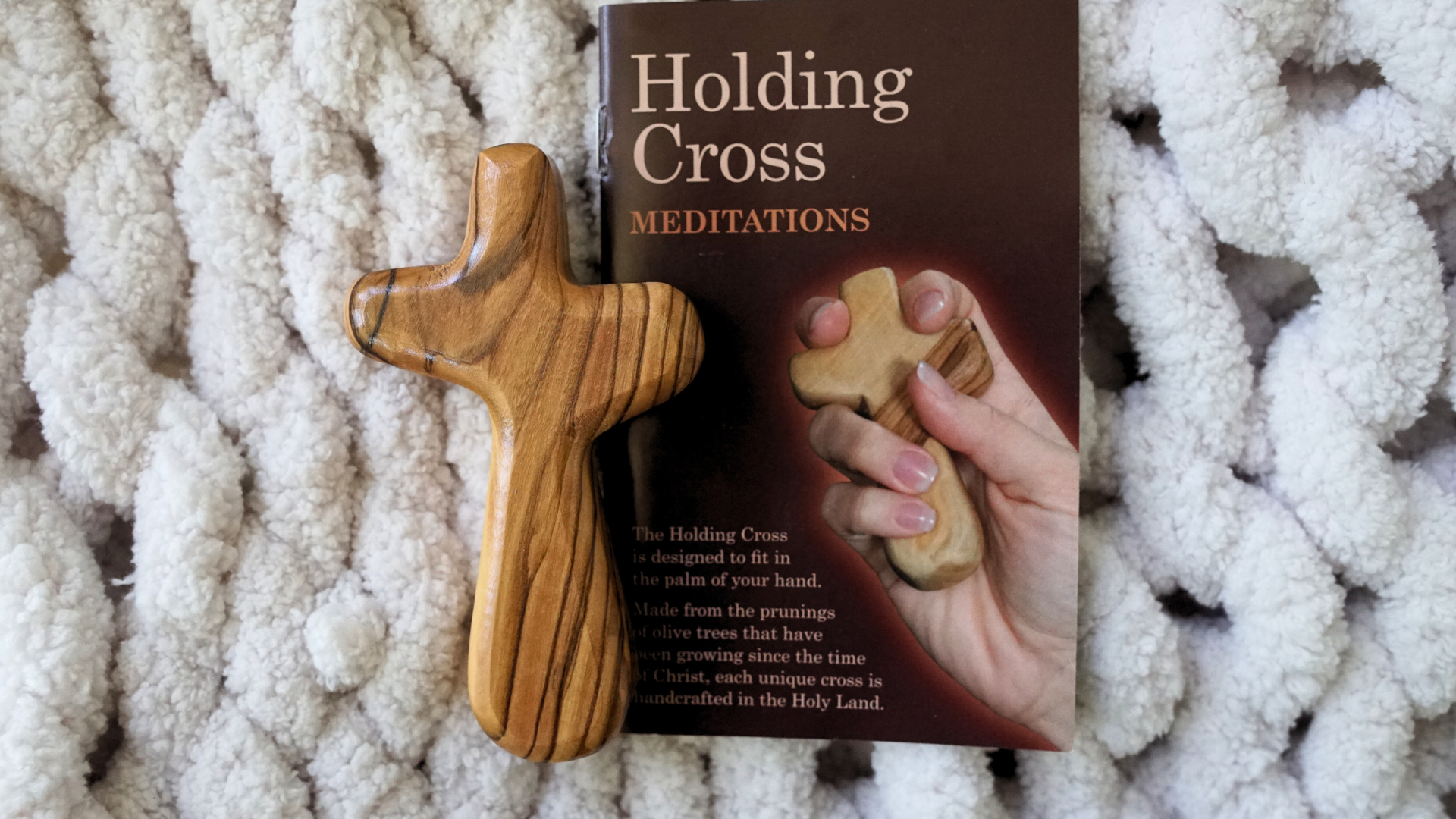 Olive wood holding cross next to meditation booklet