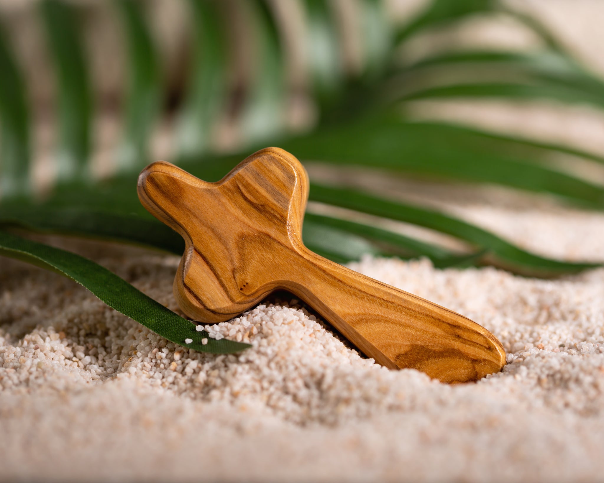 Olive wood cross in sand with palm leaves